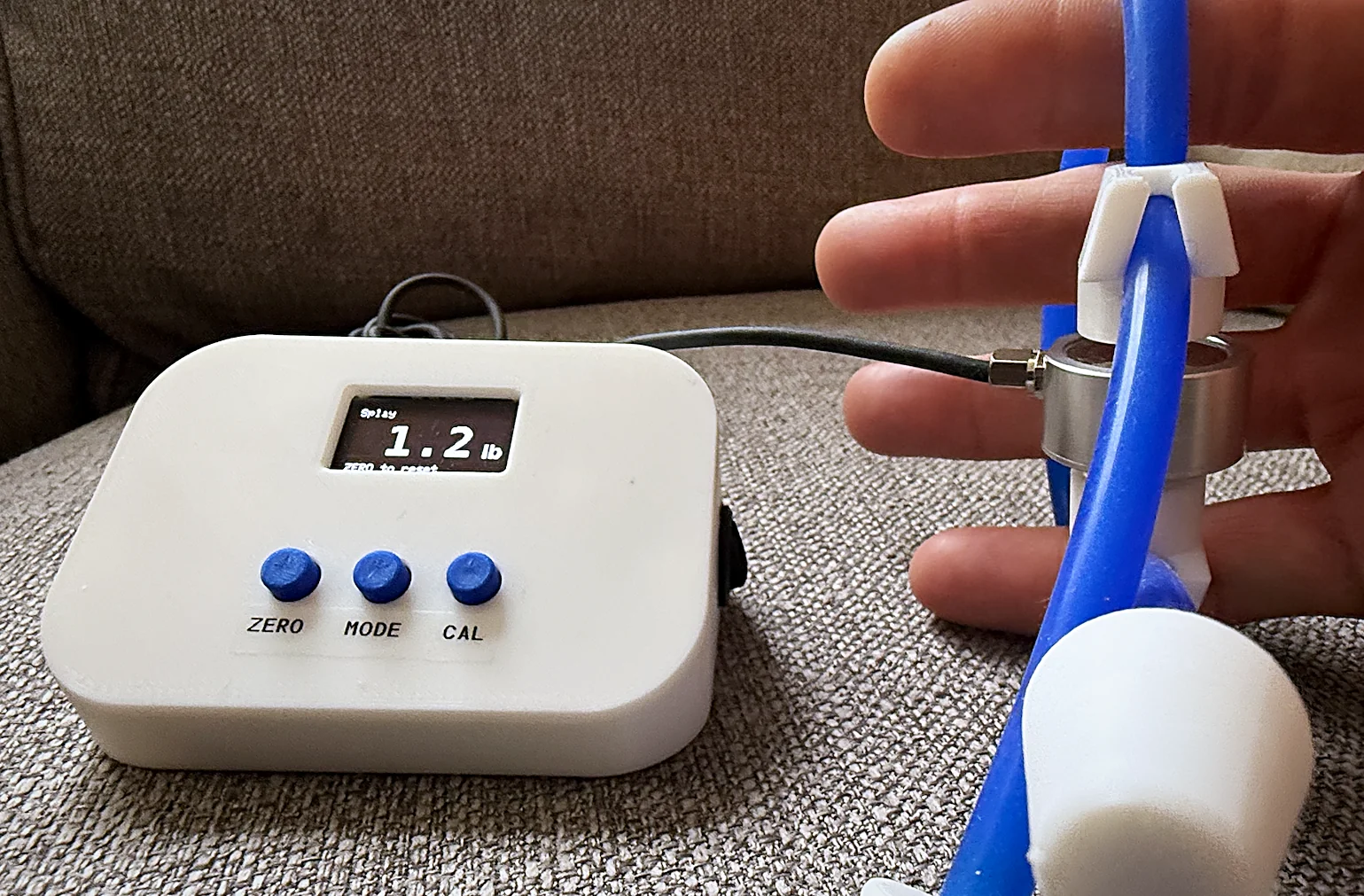 Hand inside the Splayometer hand loop attachment with the device displaying a real-time force reading